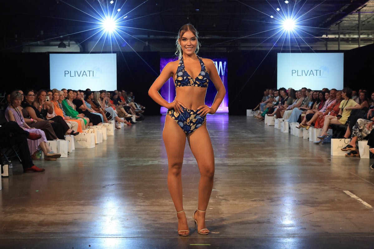 Model poses hands on hips on the runway wearing the OLIVIA Čiovo halter bikini top in navy seashell print