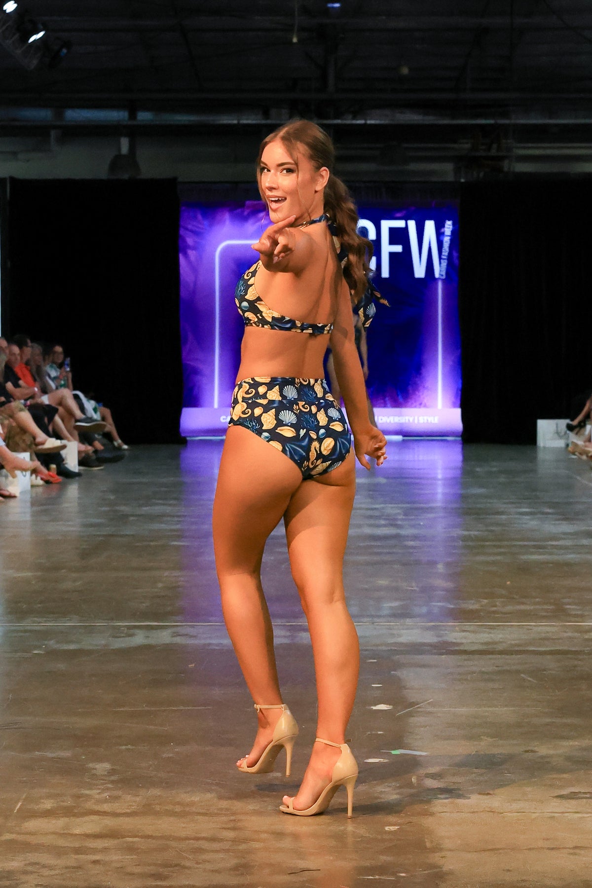 Model points to the runway audience wearing the Čiovo navy seashell print bikini set